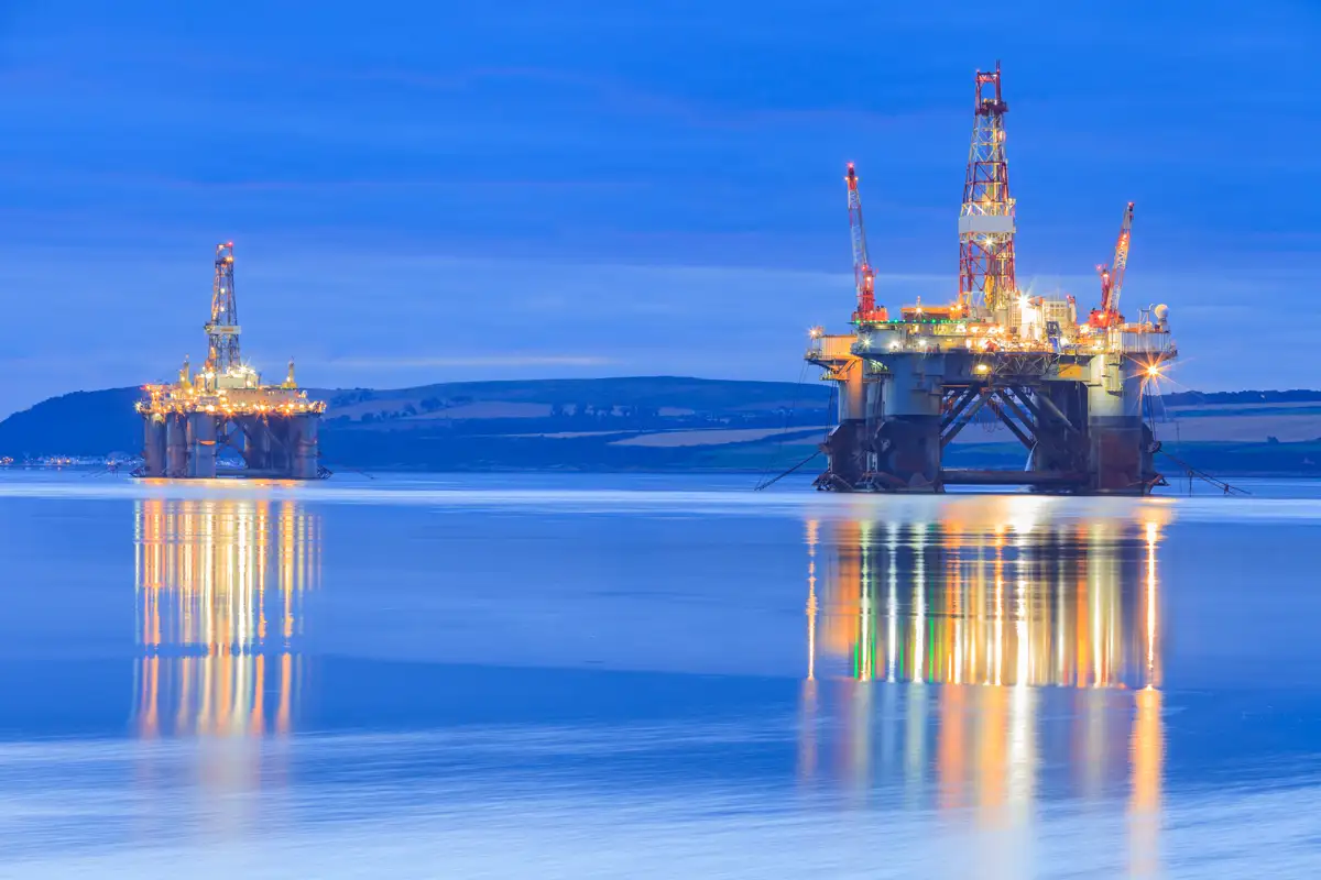 Two oil rigs offshore with lights reflecting in the water logo
